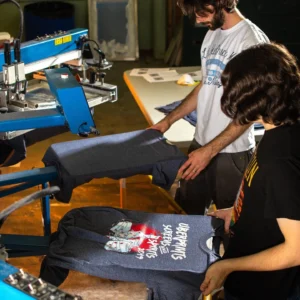 Two Lovaape team members carefully inspecting and screen-printing graphic t-shirts in our workshop